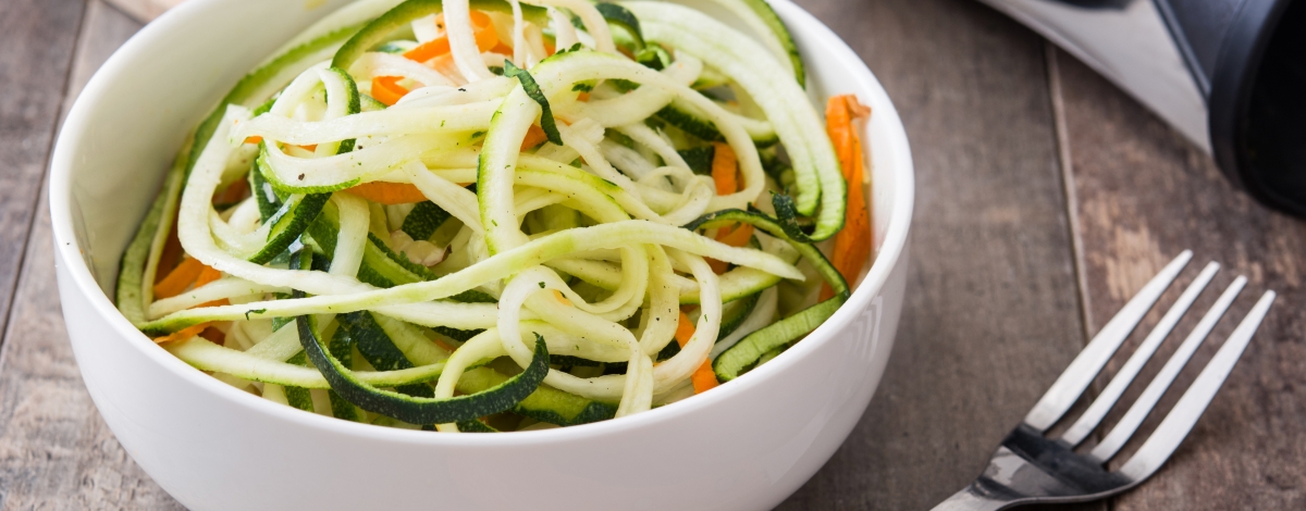 Zucchini and carrot noodles in a bowl, on wooden table